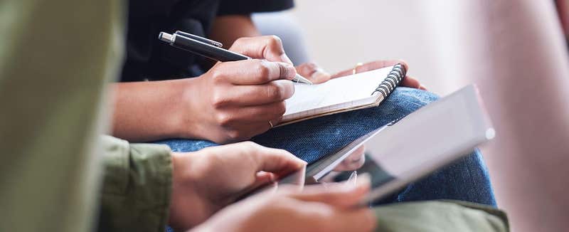 Delegates making notes in a notebook and on a tablet during a workshop