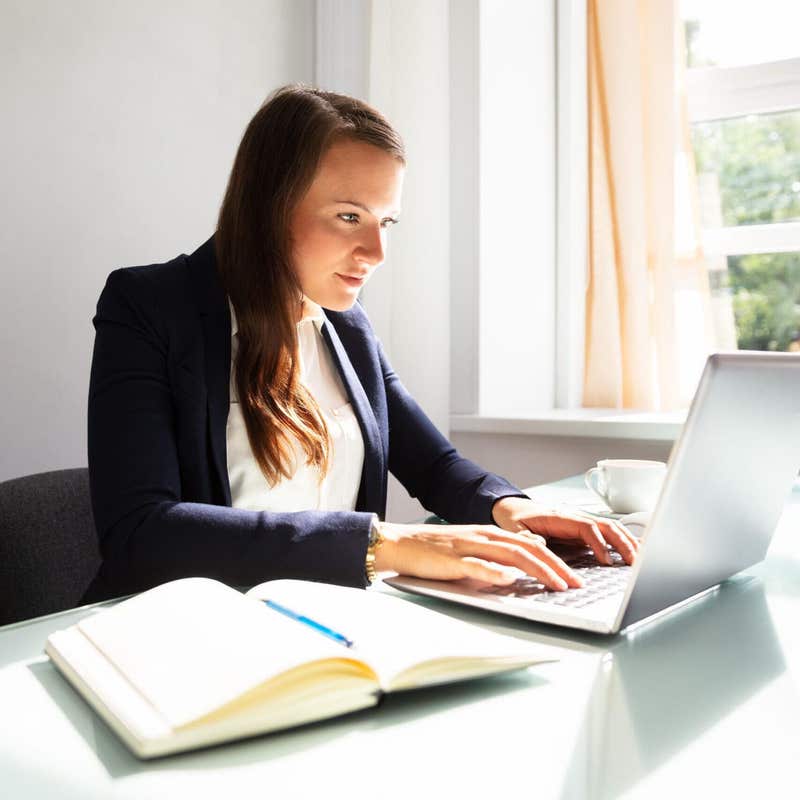 Businesswoman typing on a laptop with a notebook open on the desk