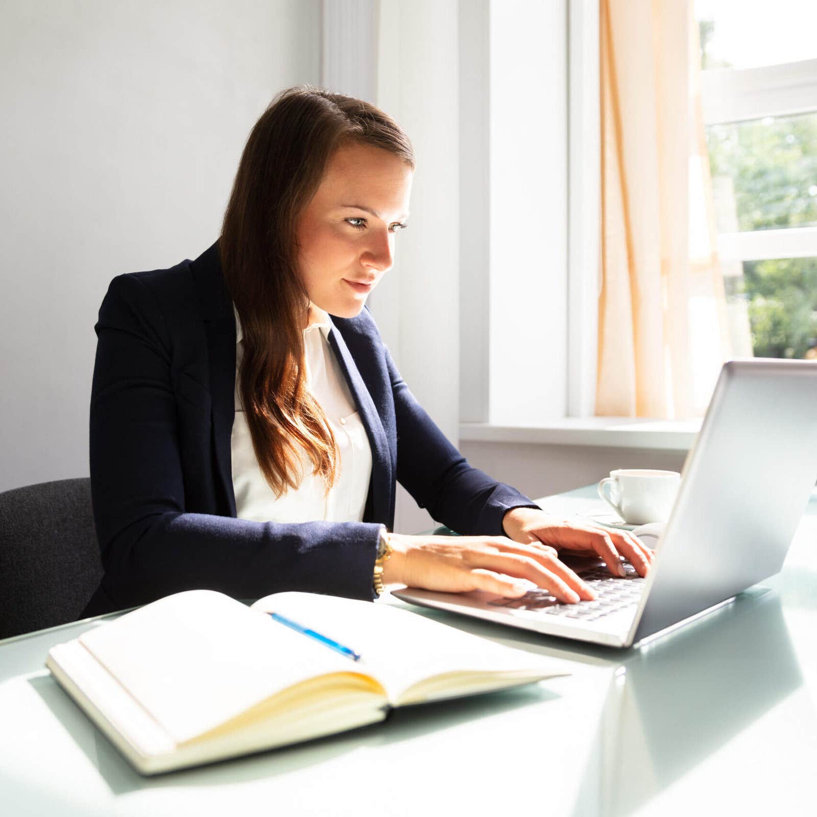 Businesswoman typing on a laptop with a notebook open on the desk
