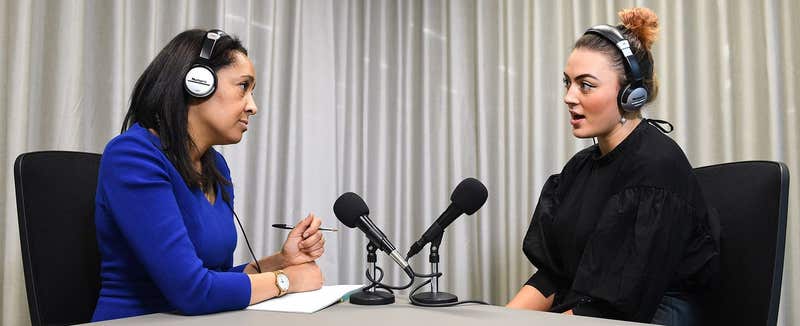 Two people recording a podcast in headphones at a studio table