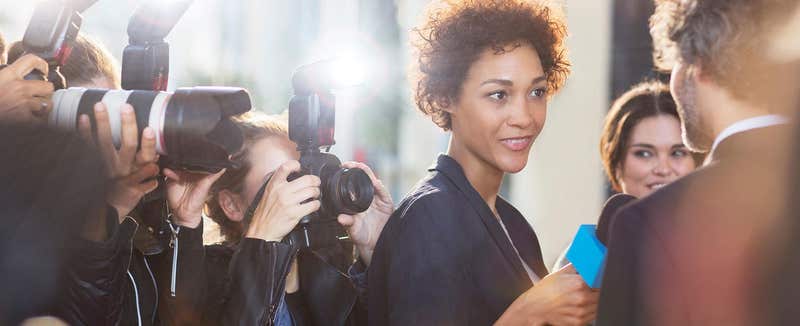 Woman speaking to a reporter in front of a bank of press photographers
