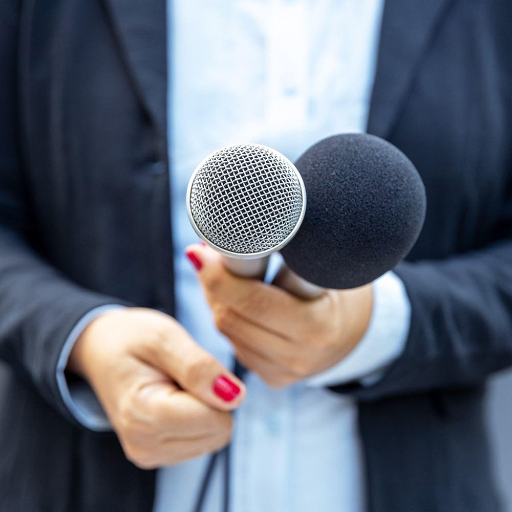 Interviewer holding two microphones towards a spokesperson