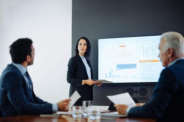 A presenter showing a data chart on a large screen to colleagues in a meeting room