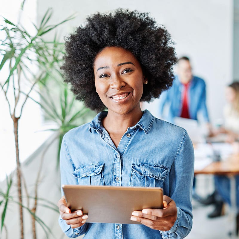 Trainee holding a tablet in a bright office with colleagues working behind