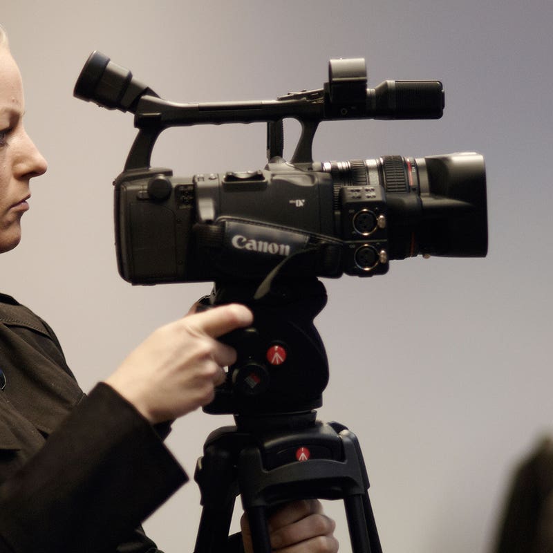 Camera operator adjusting a video camera on a tripod in a studio