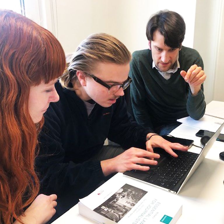 Three trainee journalists working together at a laptop with a media-law textbook open