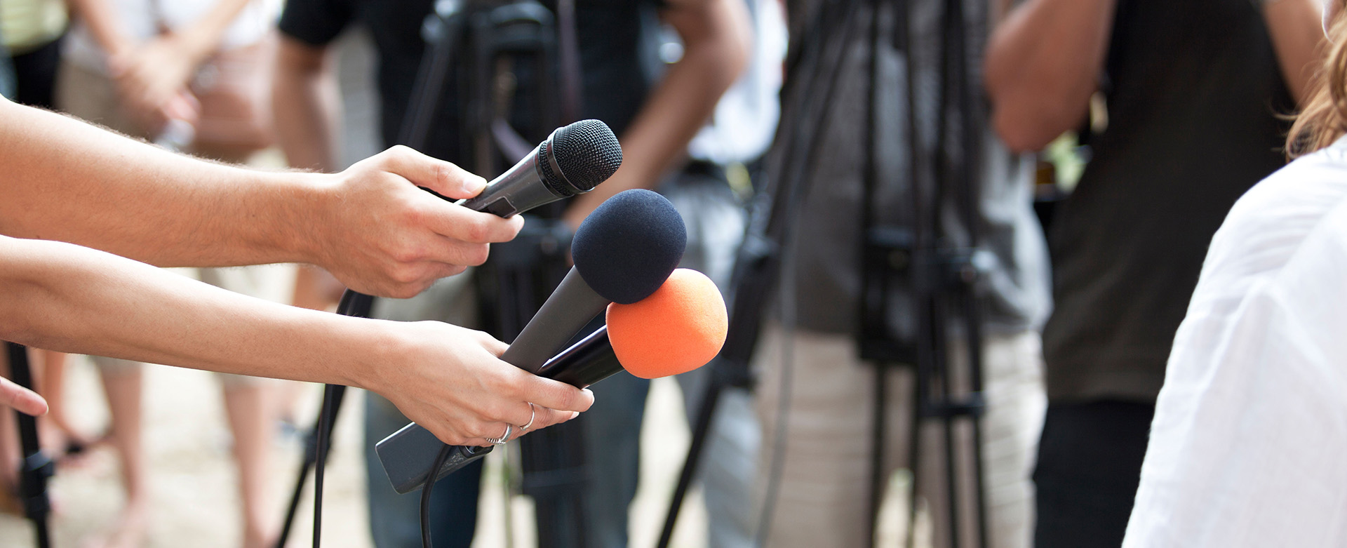 Reporters holding microphones towards an interviewee at a news event