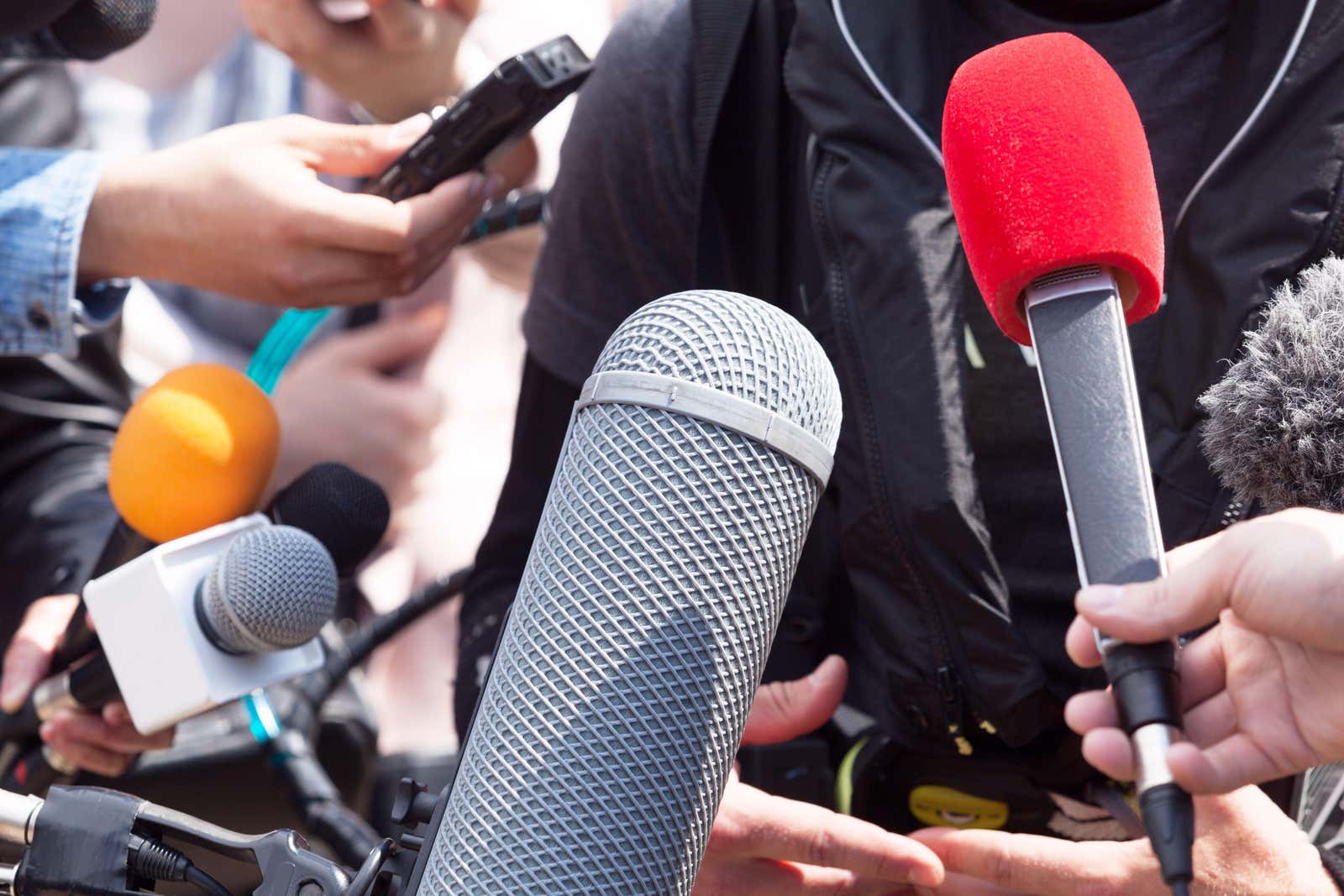 Microphones held towards a speaker at a news conference