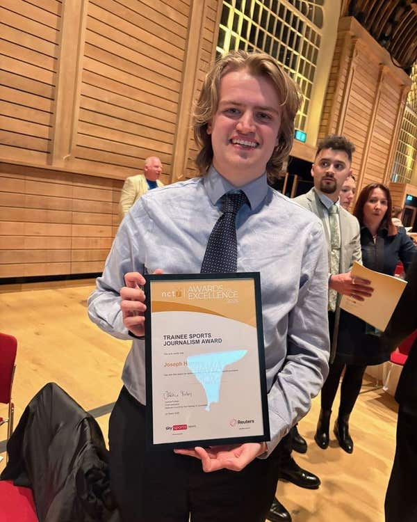 A student holding a framed journalism award certificate at an awards ceremony