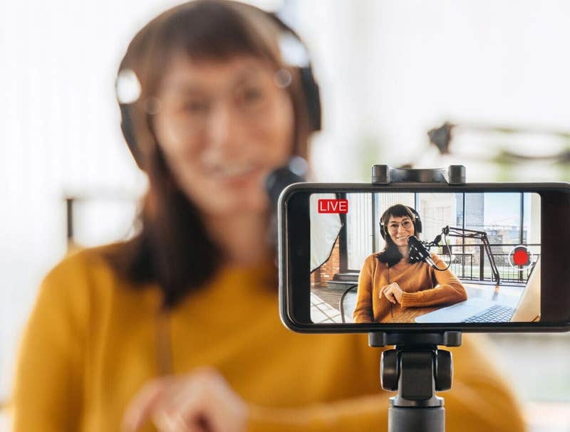 Podcast host in headphones recording a live video episode on a phone