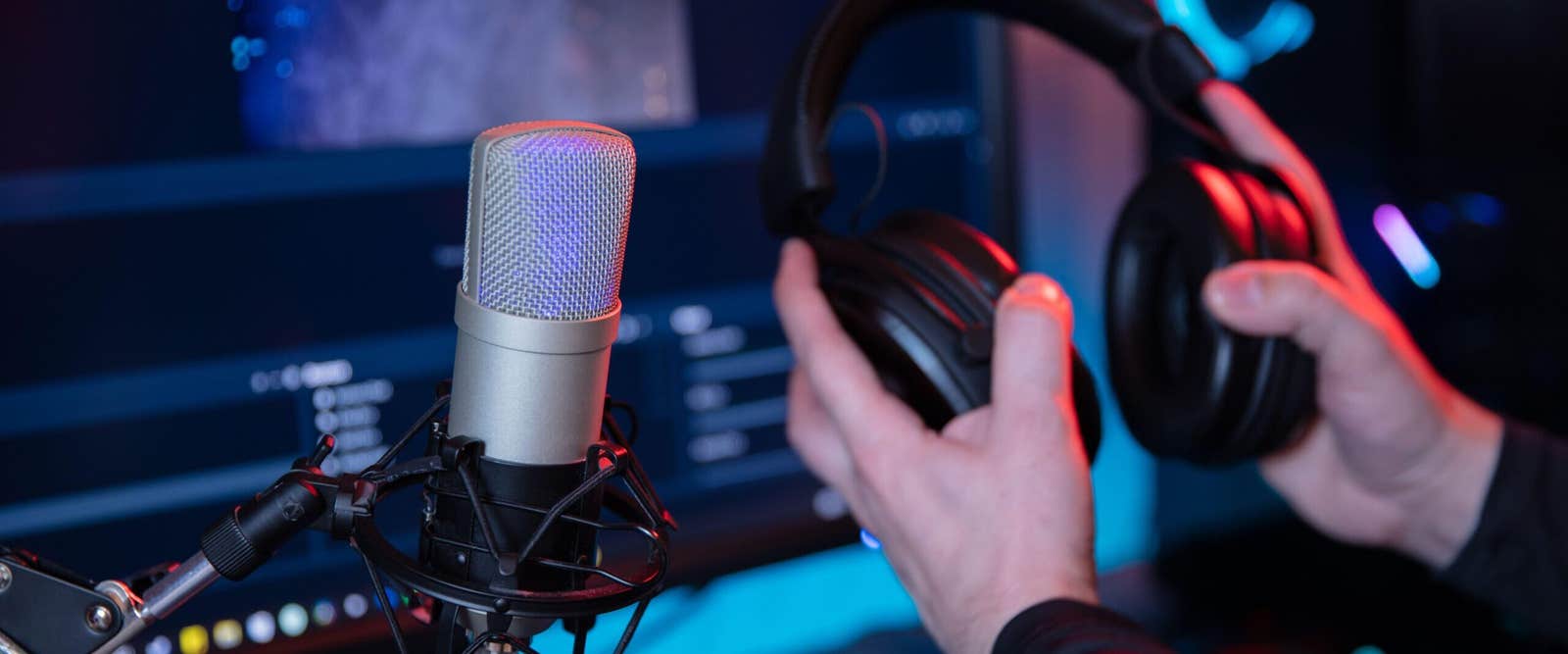 Studio microphone and headphones in a podcast studio lit in blue and red