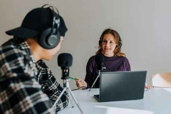 Two podcasters recording an episode with microphones, headphones and a laptop