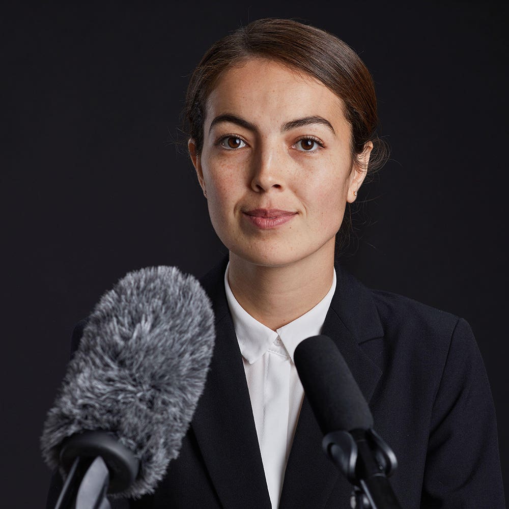 Spokesperson facing two microphones against a dark studio backdrop