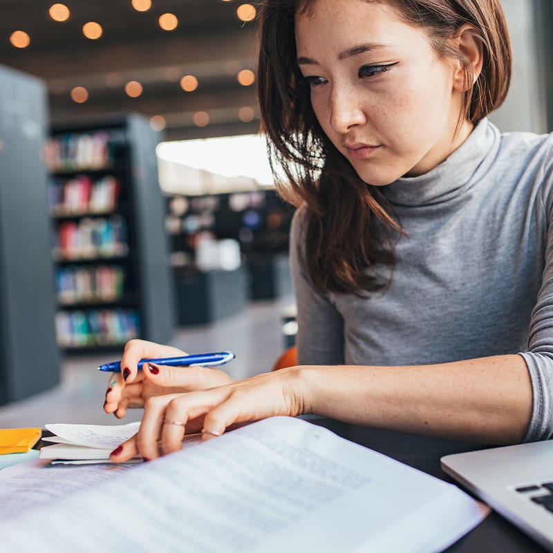 Student making notes from a textbook in a library