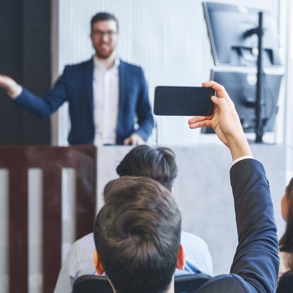 Delegate filming a speaker at a lectern on a phone