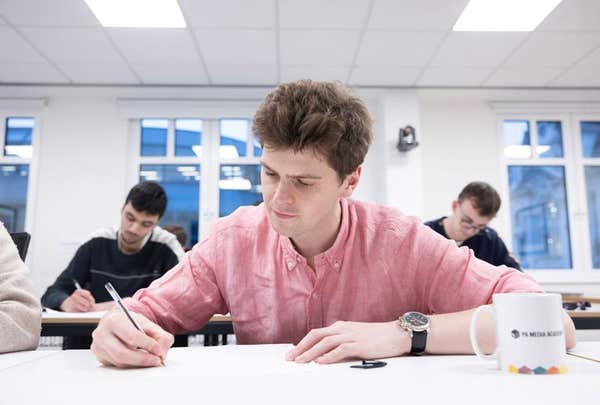 A student writing notes at a desk in a Press Association Academy classroom