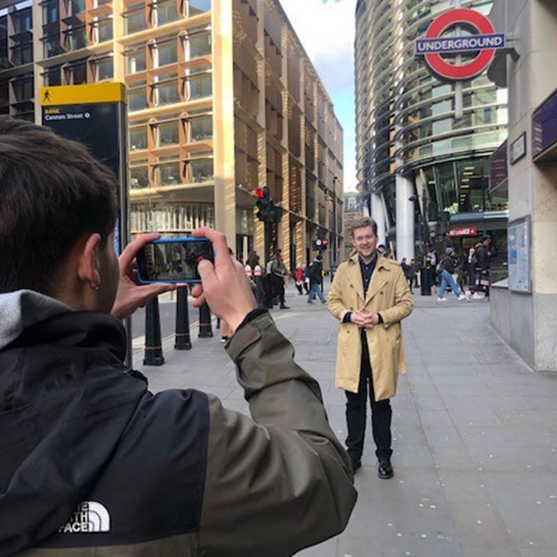 Trainee filming a fellow student presenting to camera outside a London Underground station