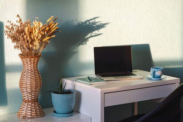3EY4NYX Laptop on desk with notebook and coffee cup in home office. Freelance workspace setup with dried plant bouquet in bas