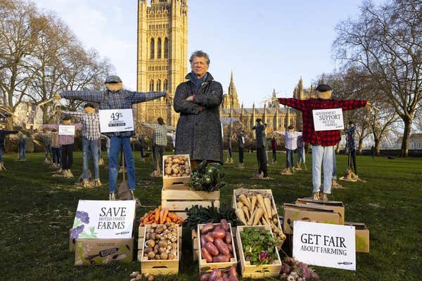 EDITORIAL USE ONLY Riverford founder Guy Singh-Watson in front of 49 scarecrows outside the Houses of Parliament in London, a
