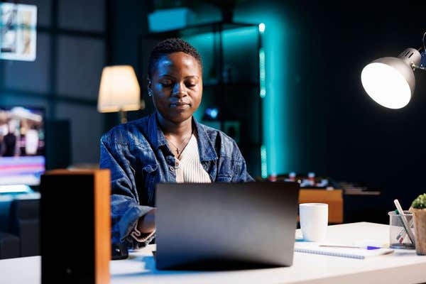 2Y849Y5 Young black woman sitting at desk and typing on digital laptop, replying to emails. African american female blogger w