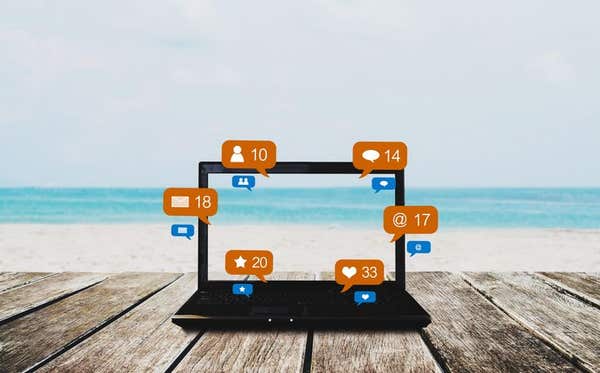 P8WM51 Computer laptop on wooden table at the beach in summer, with social media, social network notification icons