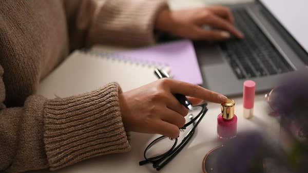 2HN80RC A female freelance makeup artist or beauty blogger creating her online beauty content, typing her cosmetics review on