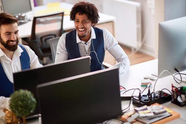 2BHERF9 colleagues watching monitor at workplace, laughing in the office. multiethnic, conversation, casual business concept