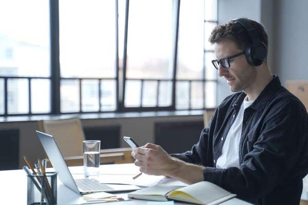 2NYJ2W2 Young german male freelancer in headphones and glasses looking at smartphone display in hands, checking last emails o