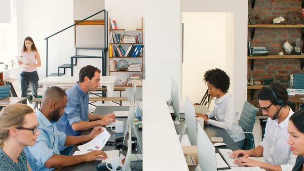 Multi-Cultural Business Team Working At Desks On Computers In Modern Open Plan Office