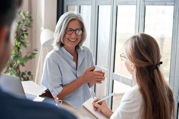 Happy old female mentor teaching young interns at group office meeting.